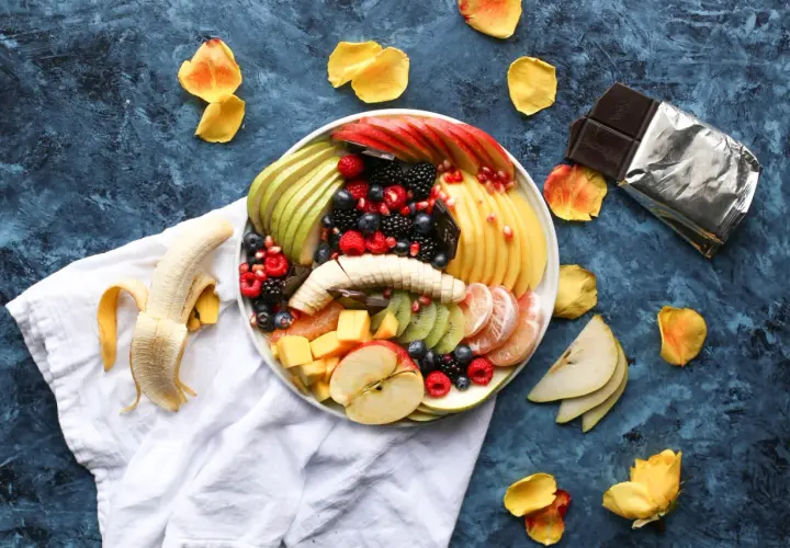 Plato de frutas variadas, incluyendo plátano, manzana, kiwi, bayas y cítricos. Es bueno comer fruta por la noche.