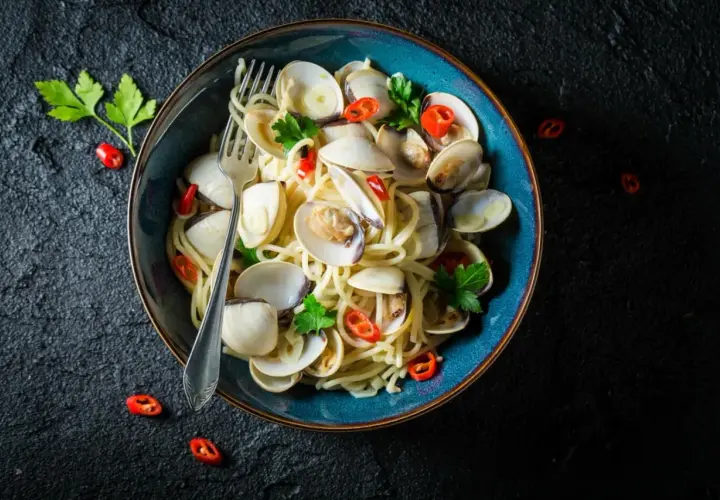 Makaron spaghetti z aromatycznymi vongole, czosnkiem i ostrą papryczką, udekorowany natką pietruszki.