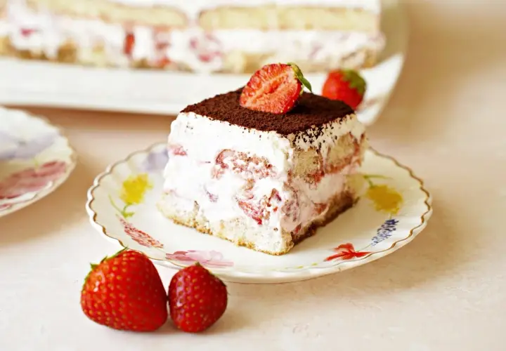 Pyszne tiramisu truskawkowe z bitą śmietaną, biszkoptami i świeżymi truskawkami, posypane kakao.