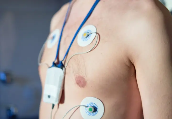 Mężczyzna z elektrodami EKG na klatce piersiowej, podłączony do urządzenia monitorującego. To właśnie holter, co to jest? Badanie serca.