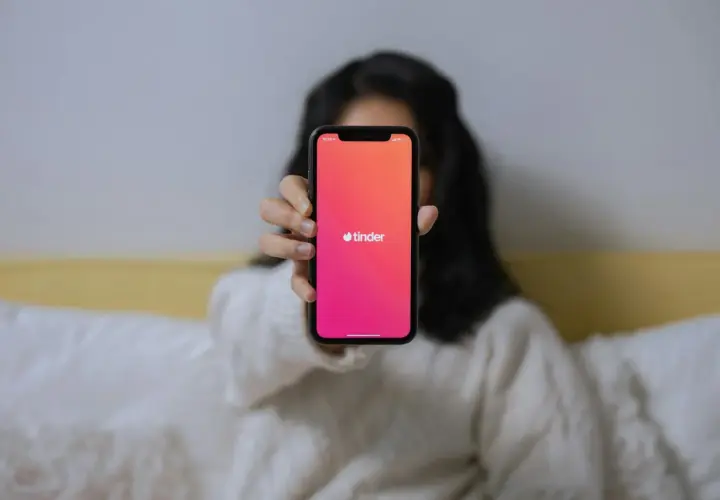 Osoba trzyma telefon z aplikacją Tinder. Chcesz wiedzieć, jak znaleźć kogoś na Tinderze?