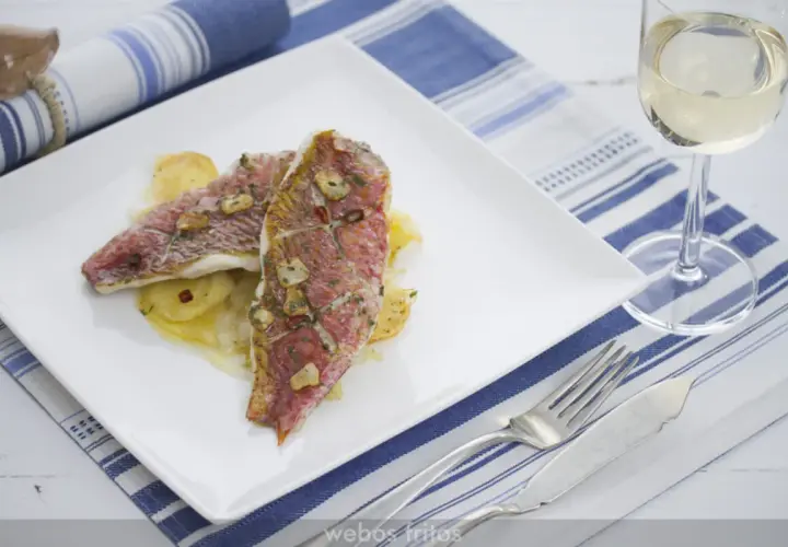 Dos deliciosos salmonetes al horno, con láminas de ajo y perejil, servidos sobre patatas. Un plato perfecto para disfrutar.