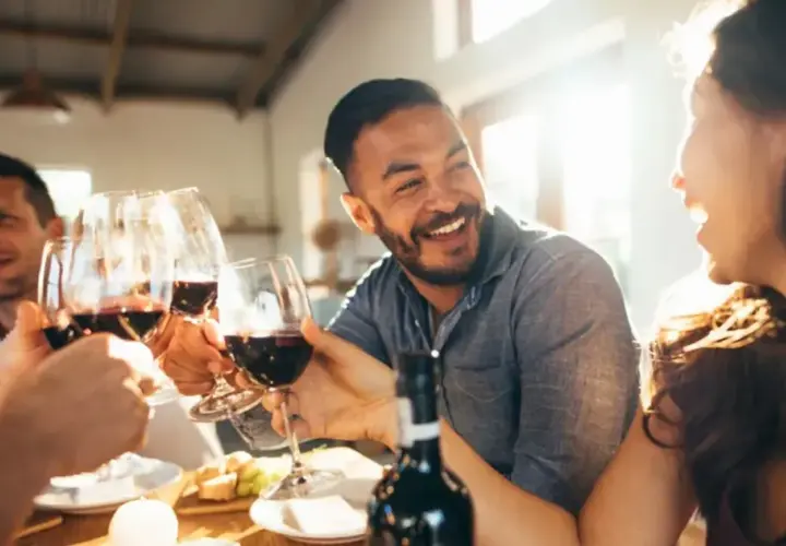 Des amis trinquent avec des verres de vin rouge lors d'une soirée dégustation vin conviviale, riant sous le soleil.