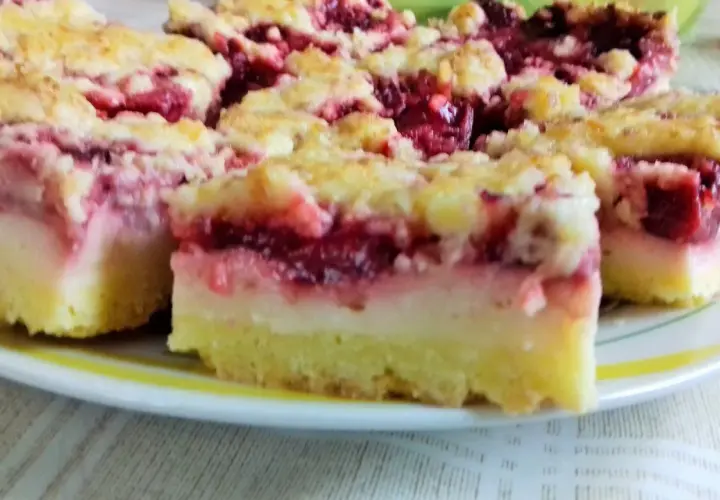 Pyszne ciasto z truskawkami i budyniem, z kruszonką na wierzchu, pokrojone na kwadraty, leży na talerzu.