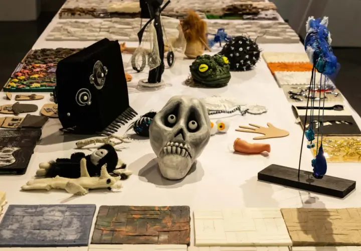 Stół pełen rekwizytów teatralnych: przerażająca czaszka, zielona żaba, czarna kamera, pluszowe zabawki i inne dziwaczne przedmioty.