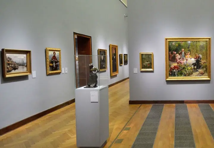 Obraz przedstawia galerię sztuki. Na ścianie wisi obraz z żydówką z pomarańczami.