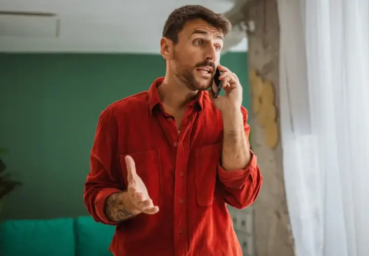 Mężczyzna w czerwonej koszuli rozmawia przez telefon, gestykulując.