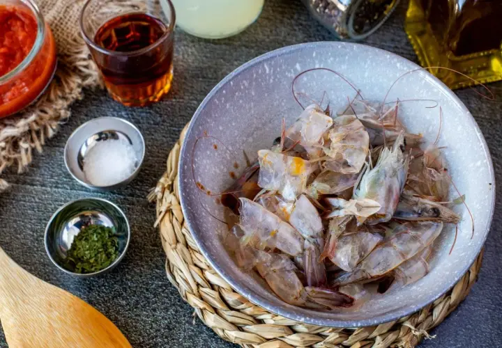 Cáscaras de camarón en un tazón, listas para hacer una sabrosa salsa americana. Ingredientes como tomate triturado, sal y hierbas acompañan.
