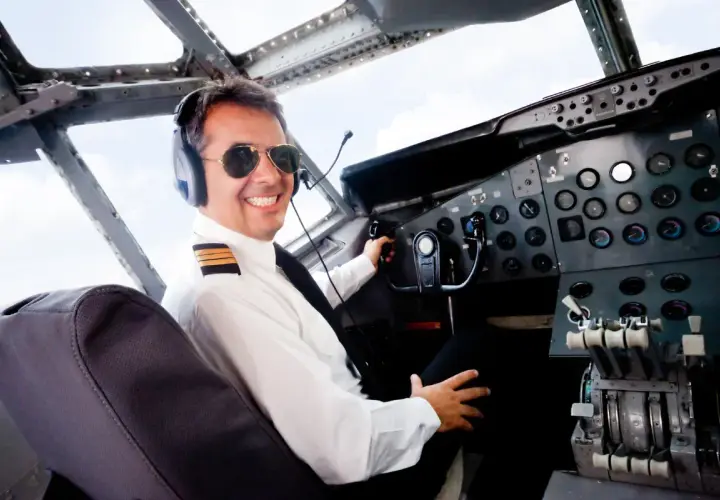 Uśmiechnięty pilot w okularach przeciwsłonecznych i słuchawkach w kokpicie samolotu. Zastanawiasz się, ile zarabia pilot samolotu?