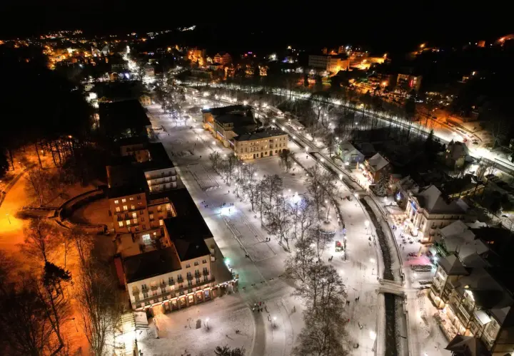 Zimowy wieczór w Krynicy-Zdroju. Oświetlone budynki i deptak przyciągają spacerowiczów, tworząc magiczną atmosferę. Krynica-Zdrój atrakcje wieczorem w śnieżnej odsłonie.