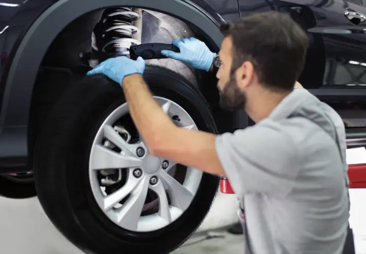 Mecánico con guantes azules revisa el amortiguador de un coche. Es importante recordar que hay que cambiar los 4 amortiguadores a la vez para un rendimiento óptimo.