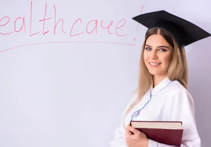 Laurea in medicina ma non voglio fare il medico. Studentessa con tocco e camice, libro in mano, davanti a una lavagna con la scritta "Healthcare".
