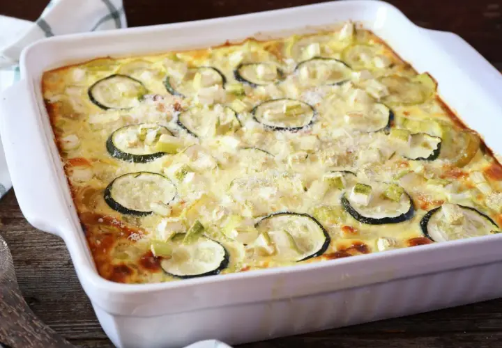 Pyszna zapiekanka z cukinii i mięsa mielonego, posypana parmezanem, w białym naczyniu żaroodpornym.