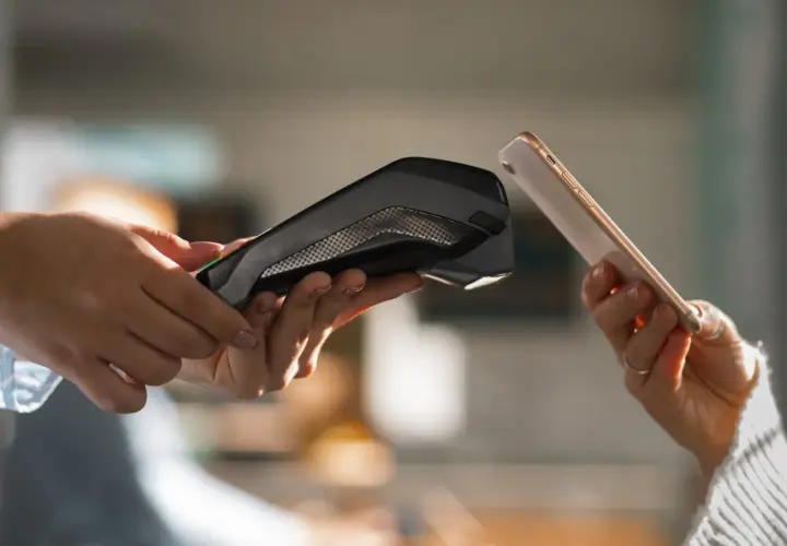 Dwie dłonie zbliżają do siebie telefon i terminal płatniczy. Pokazuje to, jak placic telefonem w prosty i szybki sposób.