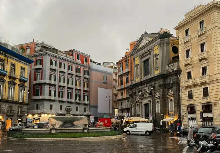 Rainy day in Naples, with colorful buildings, a fountain, and parked scooters. A perfect scene for a 2 days in Naples adventure.