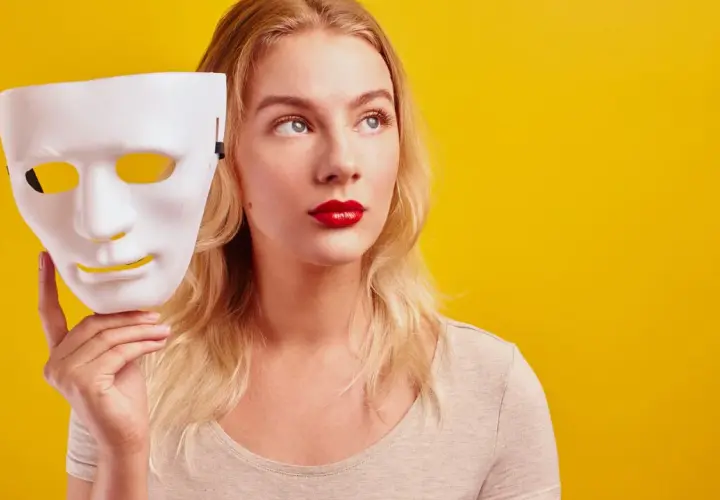 Blondynka z czerwoną szminką trzyma białą maskę, zastanawiając się nad hipokryzją.