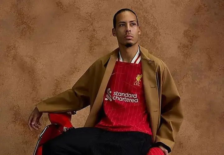 Mężczyzna w brązowej marynarce i czerwonej koszulce Liverpool z logo Standard Chartered.
