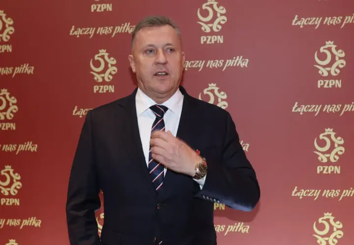 Prezes PZPN w garniturze, poprawiający krawat. Tło ozdobione logotypami PZPN i hasłem "Łączy nas piłka".