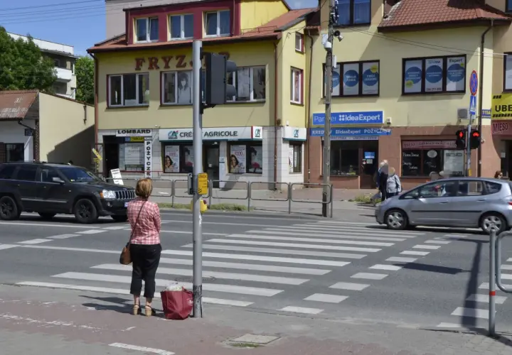 Kobieta czeka na zielone światło na pasach, kiedy należy zachować szczególną ostrożność. Samochody zbliżają się do przejścia.