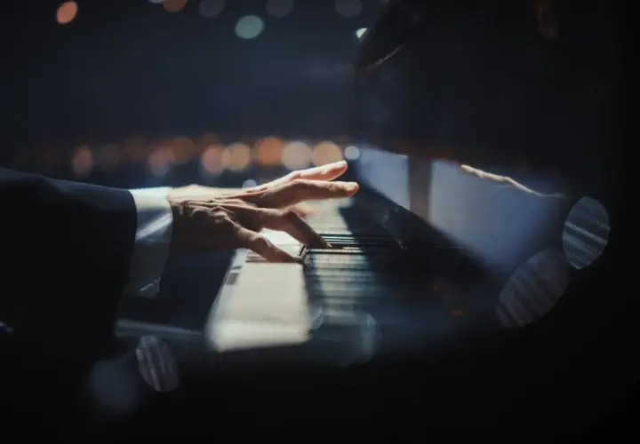 Dłoń pianisty grająca nokturn na fortepianie, w tle rozmyte światła.