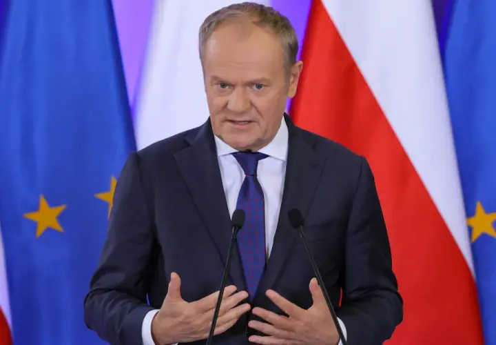 Donald Tusk w garniturze przemawia przed flagami Polski i Unii Europejskiej.
