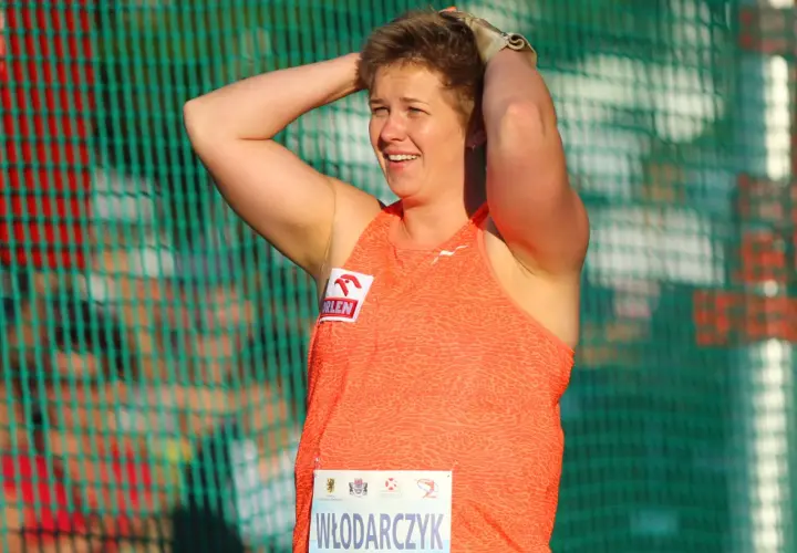 Ania Włodarczyk, po rzucie młotem rekord świata, z uśmiechem na twarzy i rękami na głowie, za zieloną siatką.