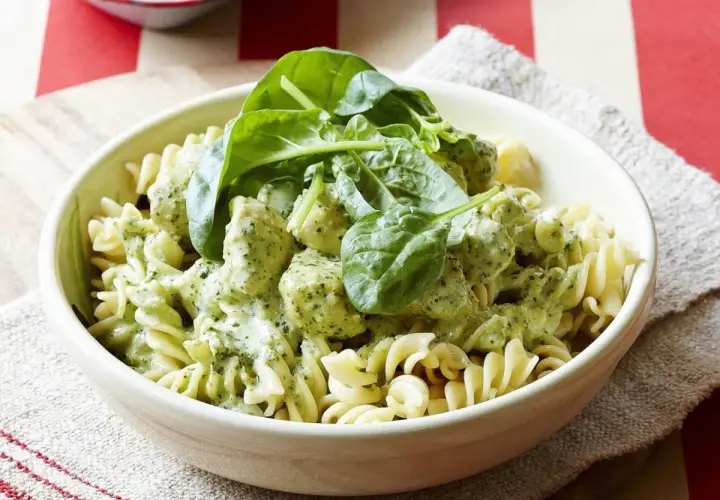Pyszny makaron z kurczakiem w kremowym sosie pesto, udekorowany świeżym szpinakiem. Idealny obiad dla całej rodziny.