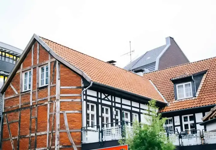 Urokliwy dom szachulcowy z ceglanymi ścianami i białymi belkami, otoczony innymi budynkami.
