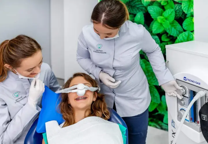 Uśmiechnięta dziewczynka z aparatem na zębach otrzymuje gaz rozweselający od dentystki, która obsługuje aparat.