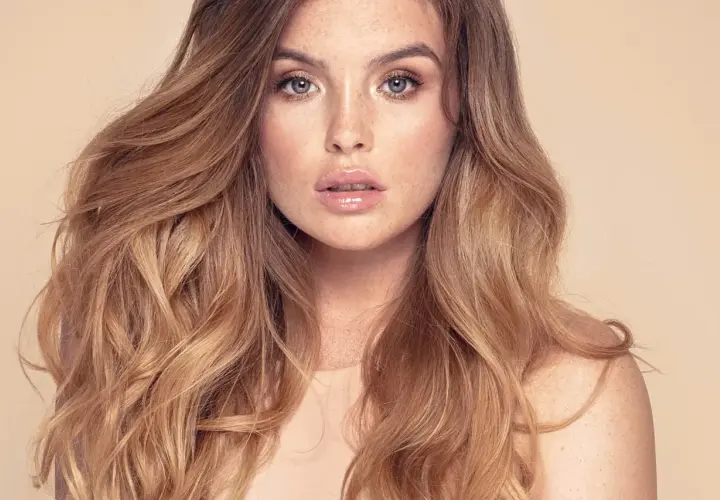 Mujer con cabello largo y ondulado, con un balayage inverso que va de castaño oscuro a rubio miel.