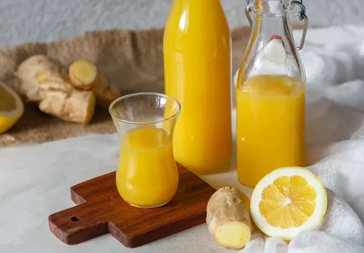 Ingwerwasser kochen oder nicht? Frischer Ingwer, Zitrone und goldgelbes Ingwerwasser in Flaschen und Glas.