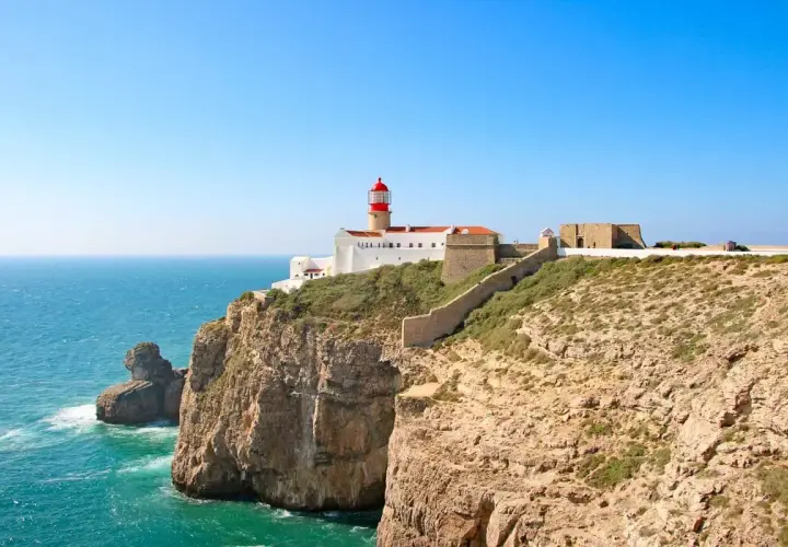 Lighthouse on a cliff overlooking the ocean, part of the fisherman's trail Portugal. Rugged coastline with a stone wall leading to the fort.