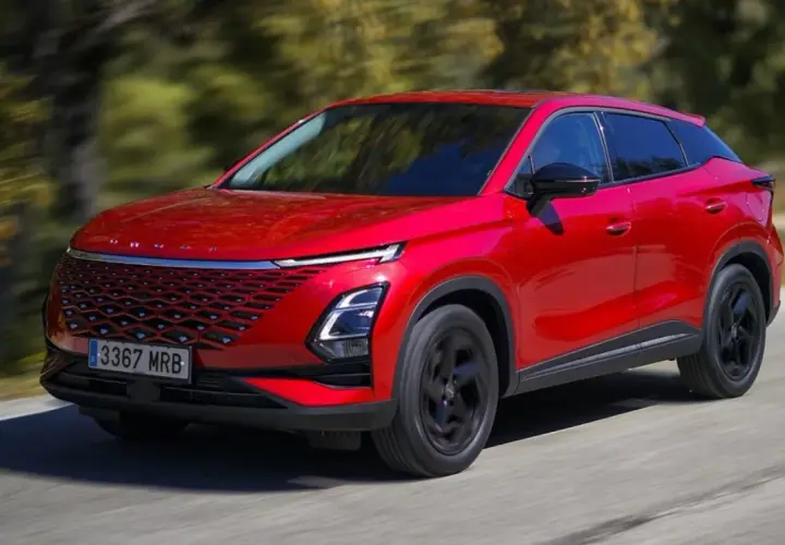 Czerwony, nowoczesny SUV, jeden z chińskich samochodów elektrycznych, jedzie po drodze wśród drzew.