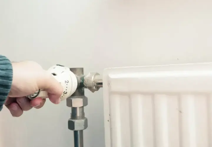 Dłoń reguluje termostat grzejnika. Po odpowietrzeniu zimny grzejnik w końcu zacznie grzać.