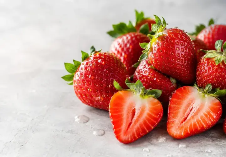 Fragole succose, ricche di potassio, su sfondo grigio. Una tagliata rivela la polpa rossa e i semini.
