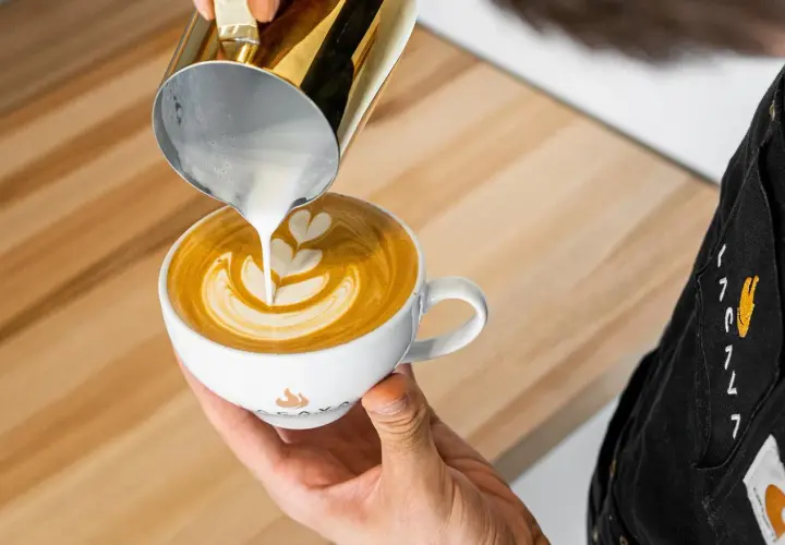Barista tworzy latte art, wlewając spienione mleko do kawy. To świetny pomysł na to, co zamiast mleka do kawy, gdy szukasz czegoś innego.