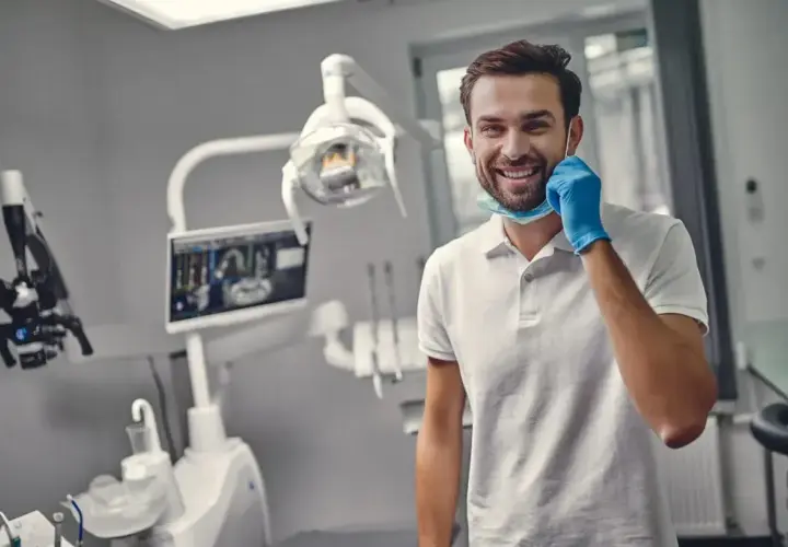 Uśmiechnięty dentysta w gabinecie, gotowy do pracy. Zastanawiasz się, ile trwa plombowanie zęba? Krótka wizyta i zdrowy uśmiech!