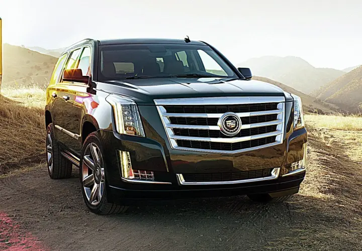 Ciemny Cadillac Escalade na tle gór i suchej trawy.