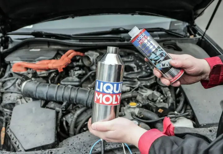 Ręce trzymają preparat do czyszczenia katalizatora diesel marki Liqui Moly. W tle widać silnik samochodu.
