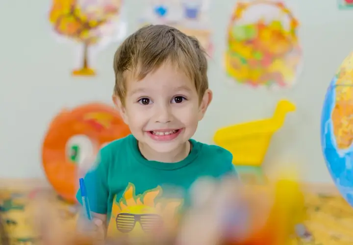 Niño sonriente con camiseta verde, rodeado de objetos coloridos. Fomenta la autoestima en niños con actividades creativas.