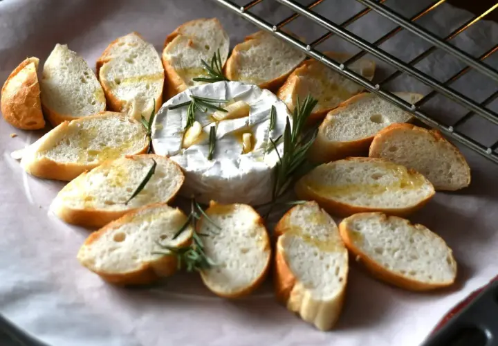 Pyszny, pieczony camembert z czosnkiem i rozmarynem, otoczony kromkami bagietki. Idealna przekąska na ciepło.
