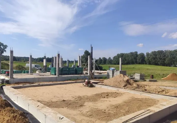 Budowa domu w toku. Widać fundamenty, betonowe słupy i hałdy piasku, który czeka na zagęszczenie.