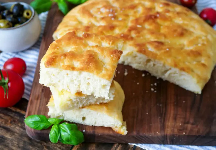 Frisch gebackene Focaccia, ein köstliches original focaccia rezept, mit Tomaten, Oliven und Basilikum auf einem Holzbrett.