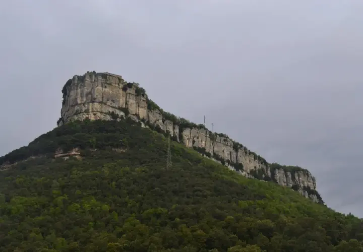 Imponent roca amb vegetació verda i una construcció al cim, recordant la Mare de Déu del Far.