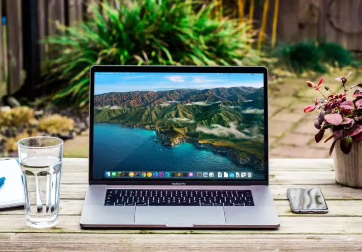 MacBook Pro z widokiem na wybrzeże Kalifornii. Obok szklanka wody, notatnik i telefon. Wiele marek laptopów oferuje podobne możliwości.