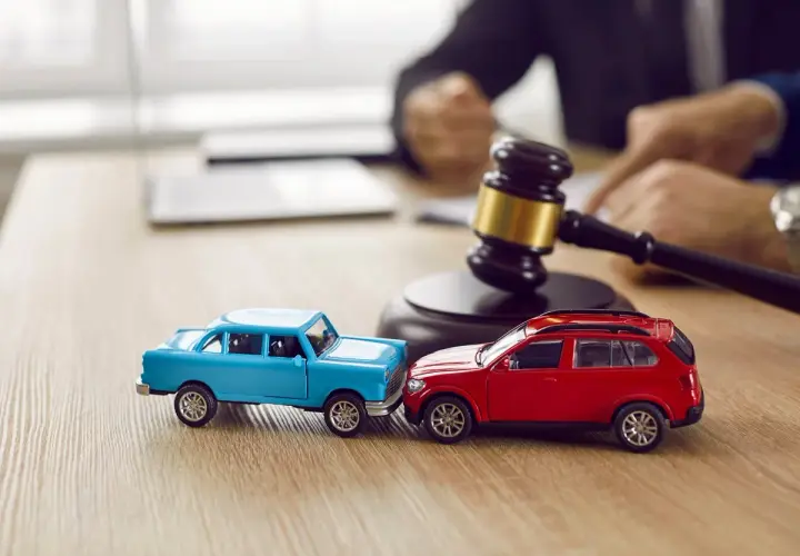 Modellini di auto blu e rossa che simulano un **infortunio in itinere** di circa 30 minuti, con un martelletto da giudice sullo sfondo.