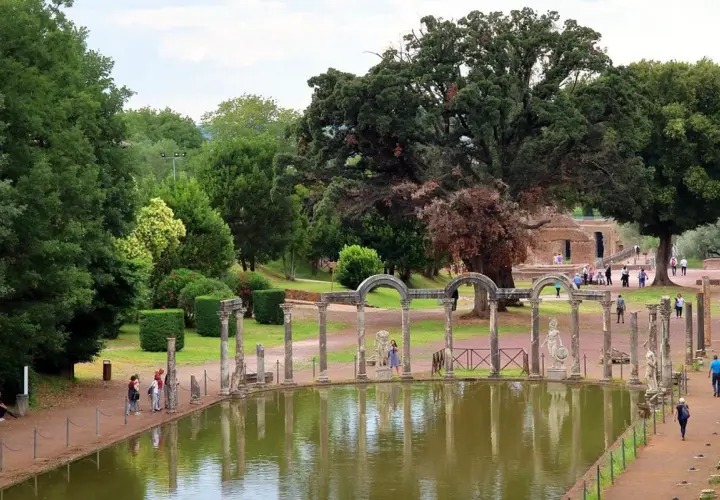 Vestiges antiques et étang reflétant le ciel à la Villa Adriana de Tivoli. Des colonnes romaines bordent l'eau, entourées de verdure luxuriante.