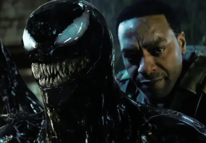 Venom, le symbiote noir aux dents acérées, se rapproche d'un homme au regard intense. Une scène prometteuse pour Venom 3.