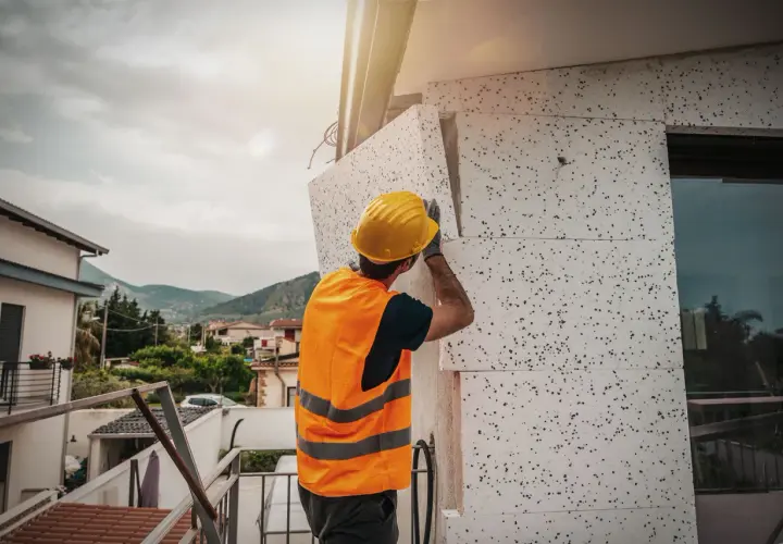 Operaio con casco giallo applica pannelli isolanti per il mini cappotto esterno di un edificio.