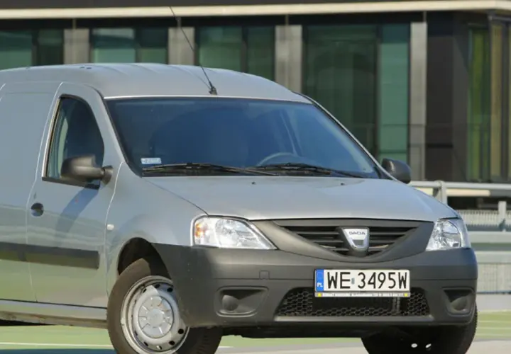 Srebrny Dacia Logan Van z polskimi tablicami WE 3495W zaparkowany przed nowoczesnym budynkiem.